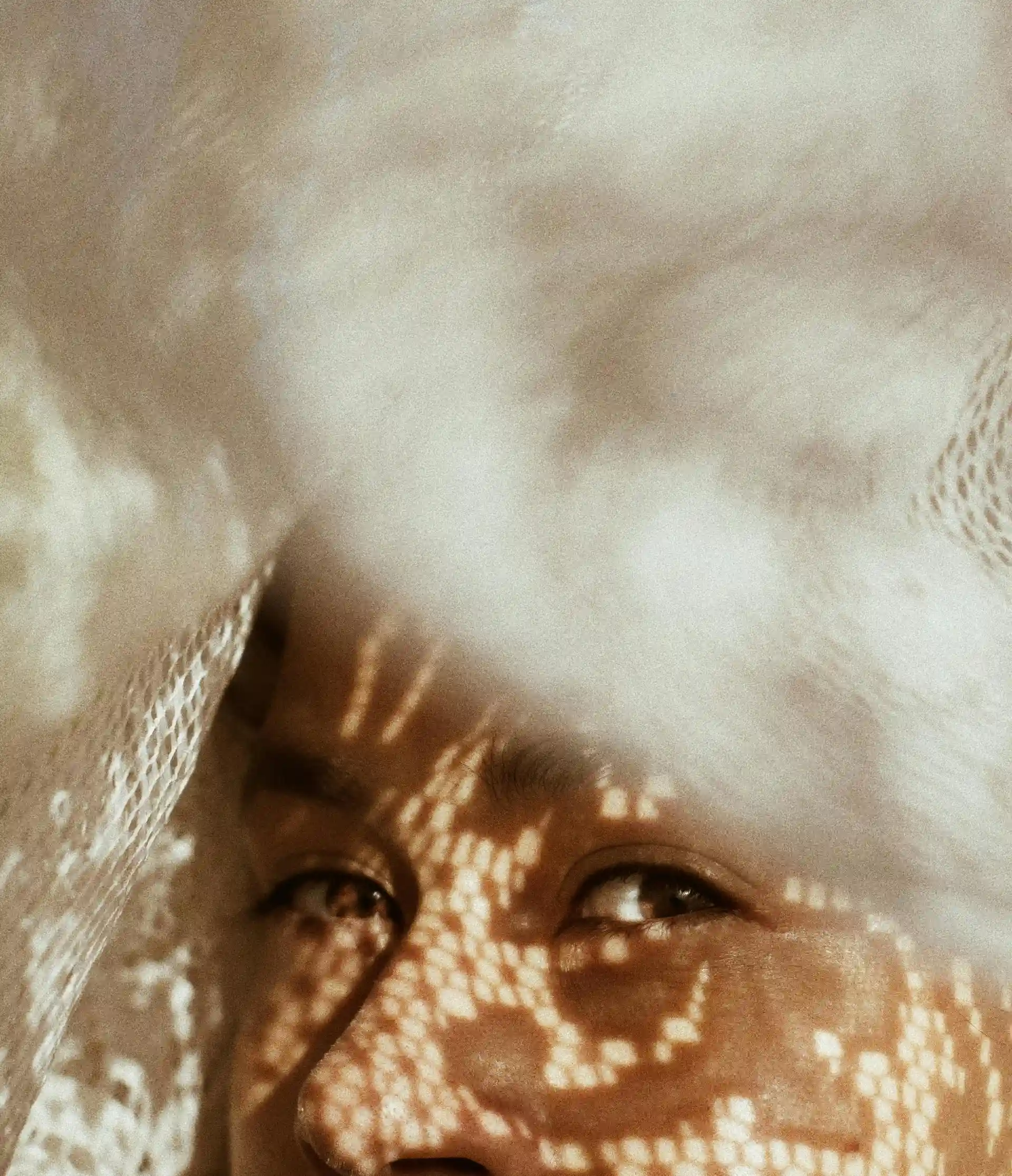 Photo portrait représentant le haut du visage d'une femme métisse aux yeux marrons, portant un voile en dentelle blanc sur la tête.
