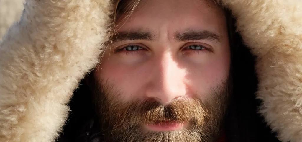 Photo portrait d'un homme barbu aux yeux bleus, portant une capuche à fourrure.